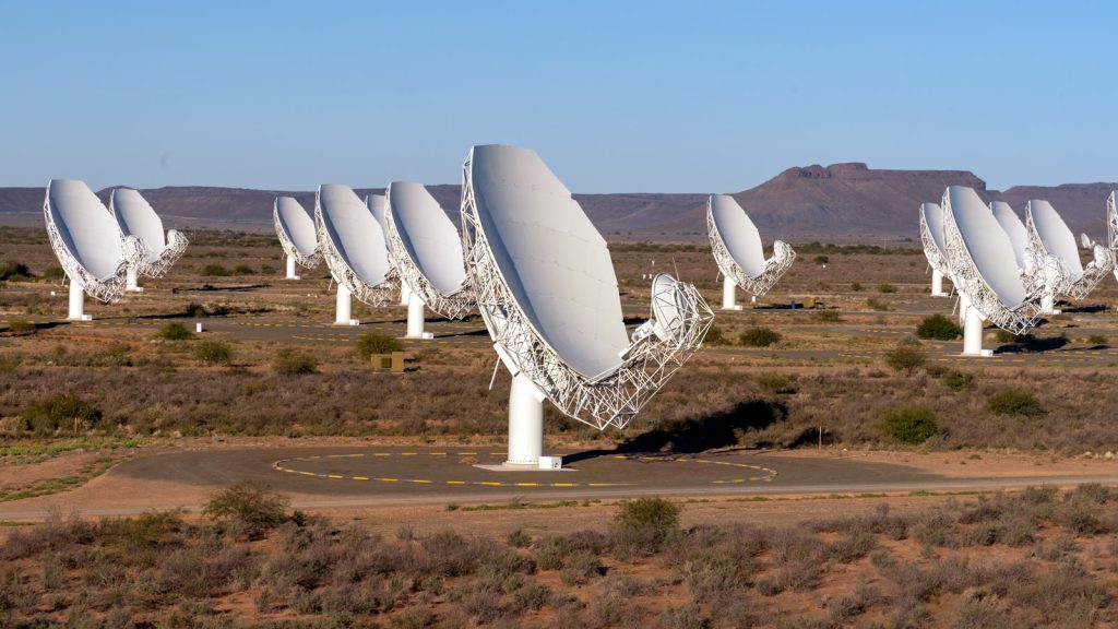 Antenas parabólicas blancas del radiotelescopio MeerKAT repartidas por la llanura semidesértica del Karoo, en Sudáfrica, bajo un cielo despejado.