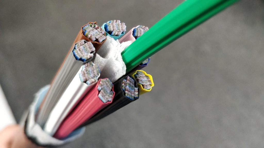 Cable de fibra óptica cortado en sección: varios tubos de colores —marrón, azul, rosa, rojo, negro, amarillo y blanco— dejan ver en su interior las cintas de fibras de vidrio apiladas.